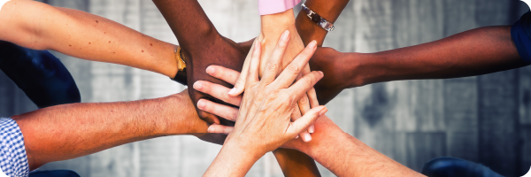 Letting family and friends know can help you stop drinking. Image shows men and women's hands of different skin tones on top of each other in a supportive gesture.