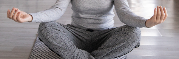Close up of a woman meditating with her legs crossed on a yoga mat.