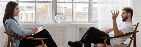 Man sitting opposite a counsellor and talking. The counsellor is holding a notepad.
