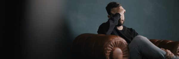 Man sat in brown leather chair, head in hands.