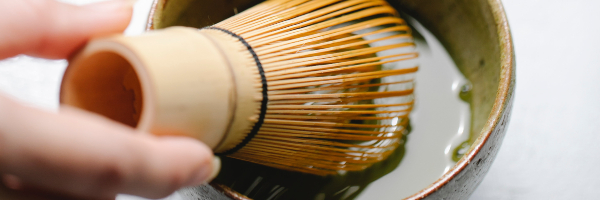 Matcha tea being stirred with a traditional whisk.