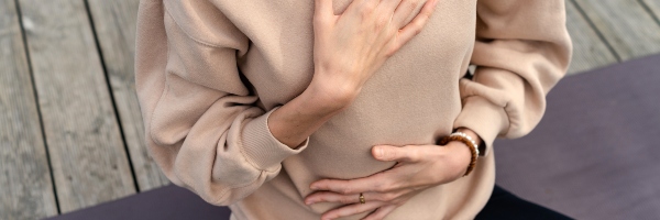 Close-up of a woman meditating on a yoga mat, a hand on her chest and stomach.