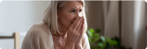A middle-aged woman sitting with her face in her hands looking pained to represent over-breathing and hyperventilation.