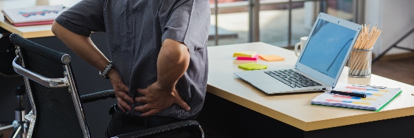 Man sat at desk with laptop, hands on lower back stretching.