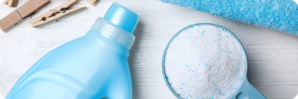 Washing detergent powder next to a blue plastic bottle and pegs and a blue towel to represent that phthalates that are often in detergents can disrupt the gut microbiome. 