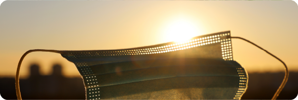 A medical face mask with the sun and sky in the background to represent that low vitamin D may be a contributory factor in an person's response to COVID-19.