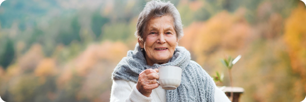 An older woman smiling holding a mug to represent that our ability to produce vitamin D declines with age.