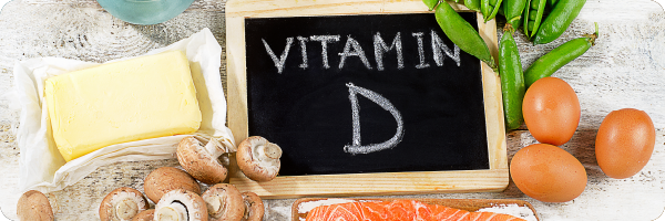 Vitamin D written on a chalkboard surrounded by vitamin D rich foods like eggs, mushrooms and salmon to represent how diet can be a source of vitamin D. 