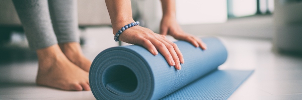 A woman rolling out a blue yoga mat on the floor for yoga practice.