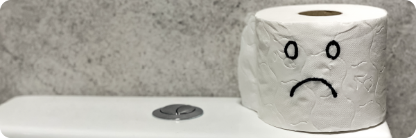 A toilet roll on a toilet tank with a sad face drawn on in black to represent constipation can affect the gut microbiome. 