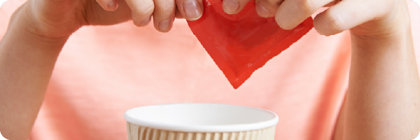 A person putting an artificial sweetener from a sachet into their drink. 