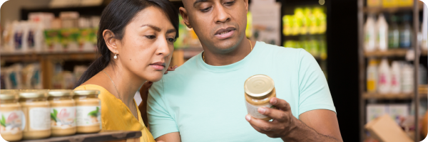 A couple looking at the label on a jar of sauce in a supermarket. 
