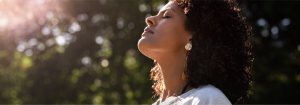 Woman nasally breathing with her eyes closed outdoors against a leafy background