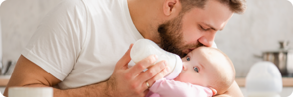 A man holding and bottle feeding a young baby milk to represent that not being breastfed can affect the gut microbiome. 