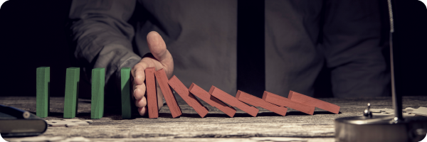 A person with a line of dominoes in front of them. Some of them are red and falling, but the person's hand is stopping the rest falling onto the green dominos to represent the concept of prevention.