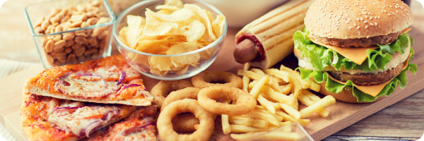 Processed foods high in carbohydrates including pizza, onion rings, French fries, a burger, crips and nuts to convey that a diet of sugar/highly refined carbohydrates and processed foods can affect the gut microbiome. 