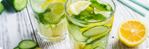A glass of water with cucumber, herbs and lemon slices.