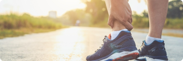 Person wearing running trainers holding their injured ankle.