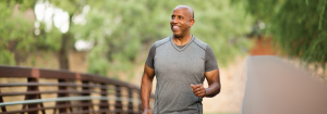 A smiling man running outdoors with green trees in the background.