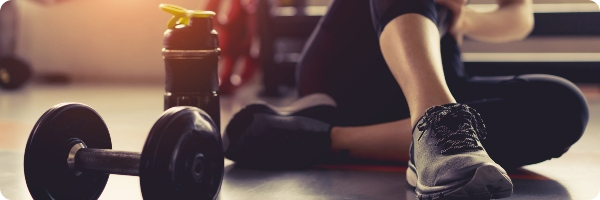 Woman's feet in trainers with dumbbell weights and a water bottle on the floor