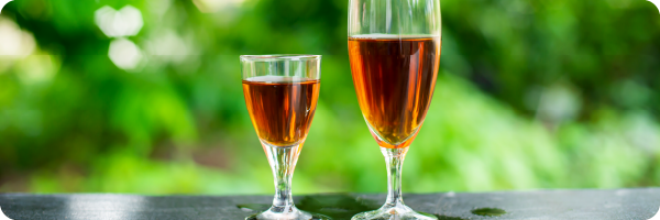 Avoid alcohol in the evenings for better sleep. Image shows a small glass of rose wine next to a bigger glass of rose wine with outdoor greenery in the background. 