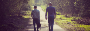 Two men walking on a path lined with grass and trees with their backs to the camera to represent talking as one of the ways to reduce the stigma surrounding mental health.