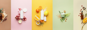 Different bottles and containers of natural skincare products on different coloured background next to natural ingredients like fruit, nuts and leaves to illustrate green beauty.