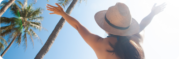 A person sunbathing next to palm trees, wearing a sunhat.