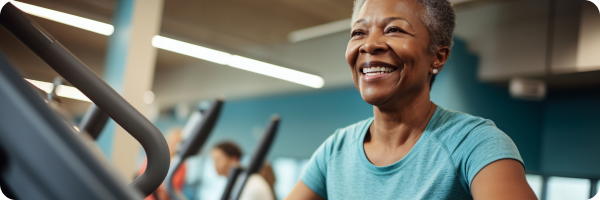 An older black woman with short grey hair is smiling and she is working out on a treadmill.