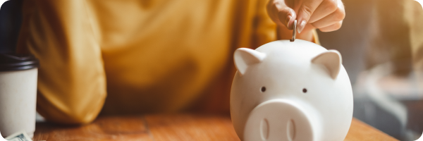 A person putting a coin into a piggy bank highlighting the financial benefits of quitting smoking. 
