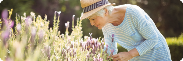 An older woman wearing a sunhat smelling some flowers outdoors on a sunny day illustrating one of the benefits of quitting smoking: regaining your sense of smell. 