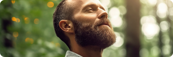 A middle-aged man looking content breathing in fresh air in the woods to represent the benefits of quitting smoking. 