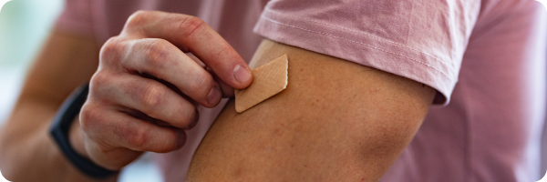 A man putting a nicotine patch on his arm to represent how stop smoking therapies can help you quit smoking. 